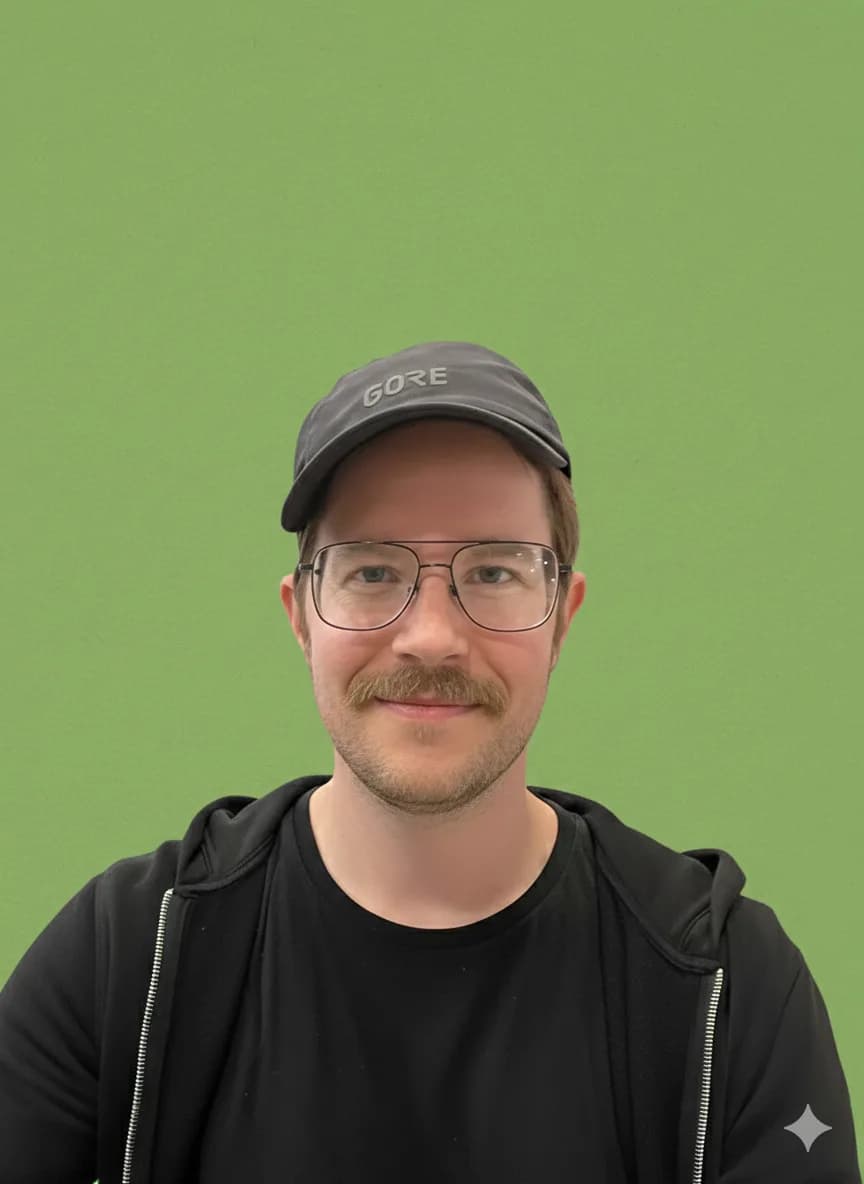 Porträt von Tony Joke: Mann mit Schildmütze, Brille und Schnurrbart vor grünem Hintergrund